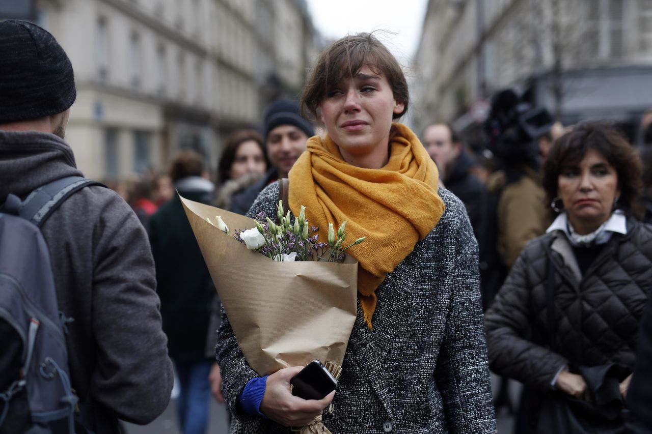 A woman carrying flowers cries in front of the Carillon cafe and the Petit Cambodge restaurant in Paris Saturday Nov. 14, 2015, a day after a series of attacks in Paris.