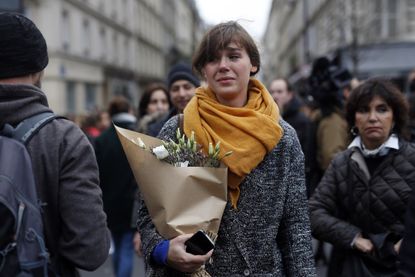 A woman carrying flowers cries in front of the Carillon cafe and the Petit Cambodge restaurant in Paris Saturday Nov. 14, 2015, a day after a series of attacks in Paris.
