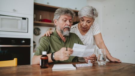 An older couple look at medication paperwork together in their kitchen.