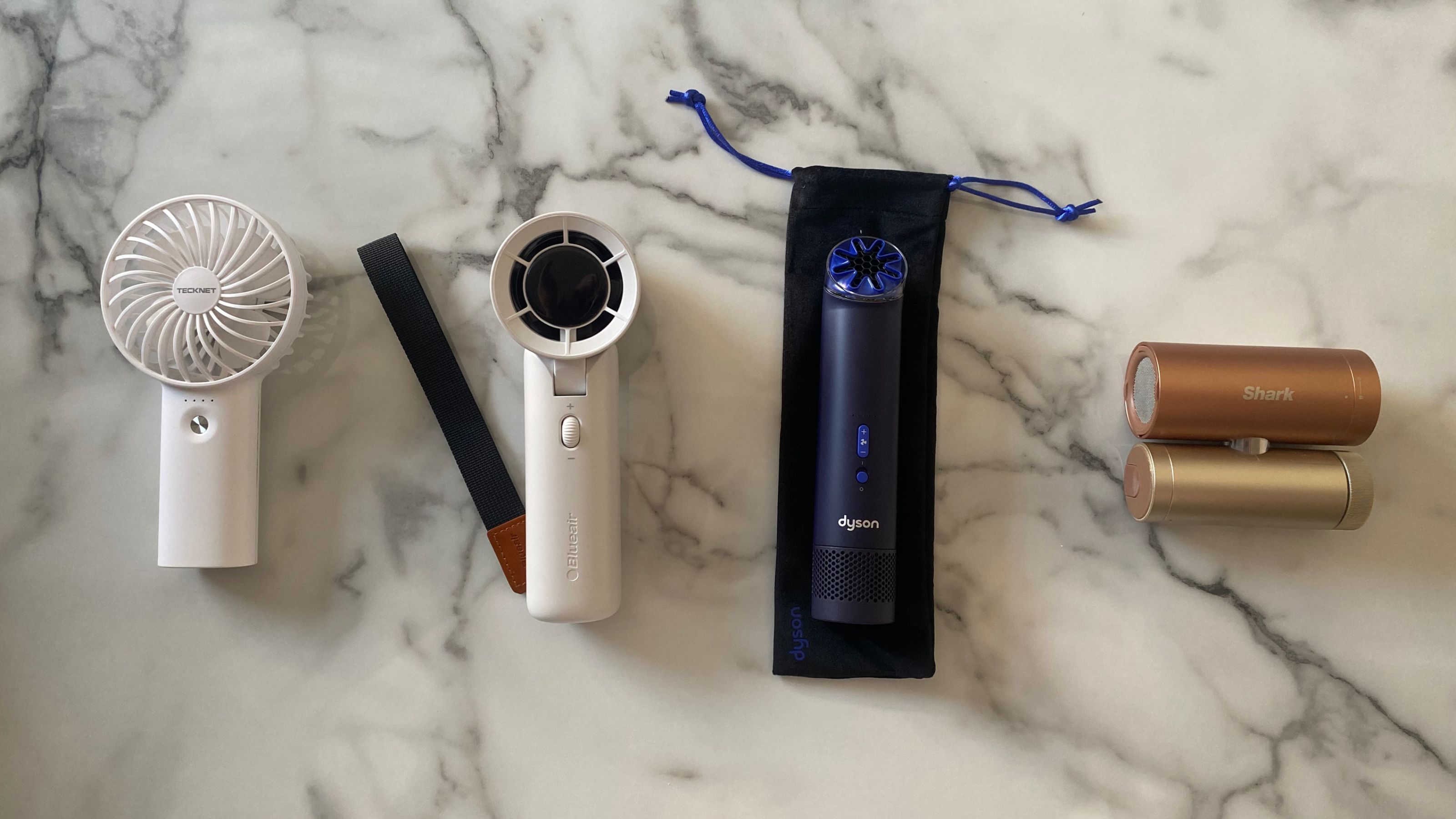 An Amazon fan, Blueair AlwaysCool Portable Handheld Fan, Dyson HushJet Mini Cool Fan and the Shark ChillPill on a white and grey marble look surface