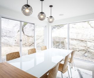 Interior view of the dining area at Float House featuring a white ceiling and walls, sphere pendant lighting. tall windows and doors, a white rectangle dining table and wooden chairs