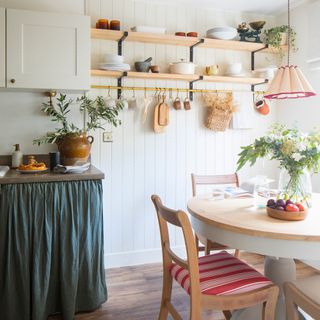 an open plan kitchen diner with a blue/green cabinet skirt, open shelving and a dining table