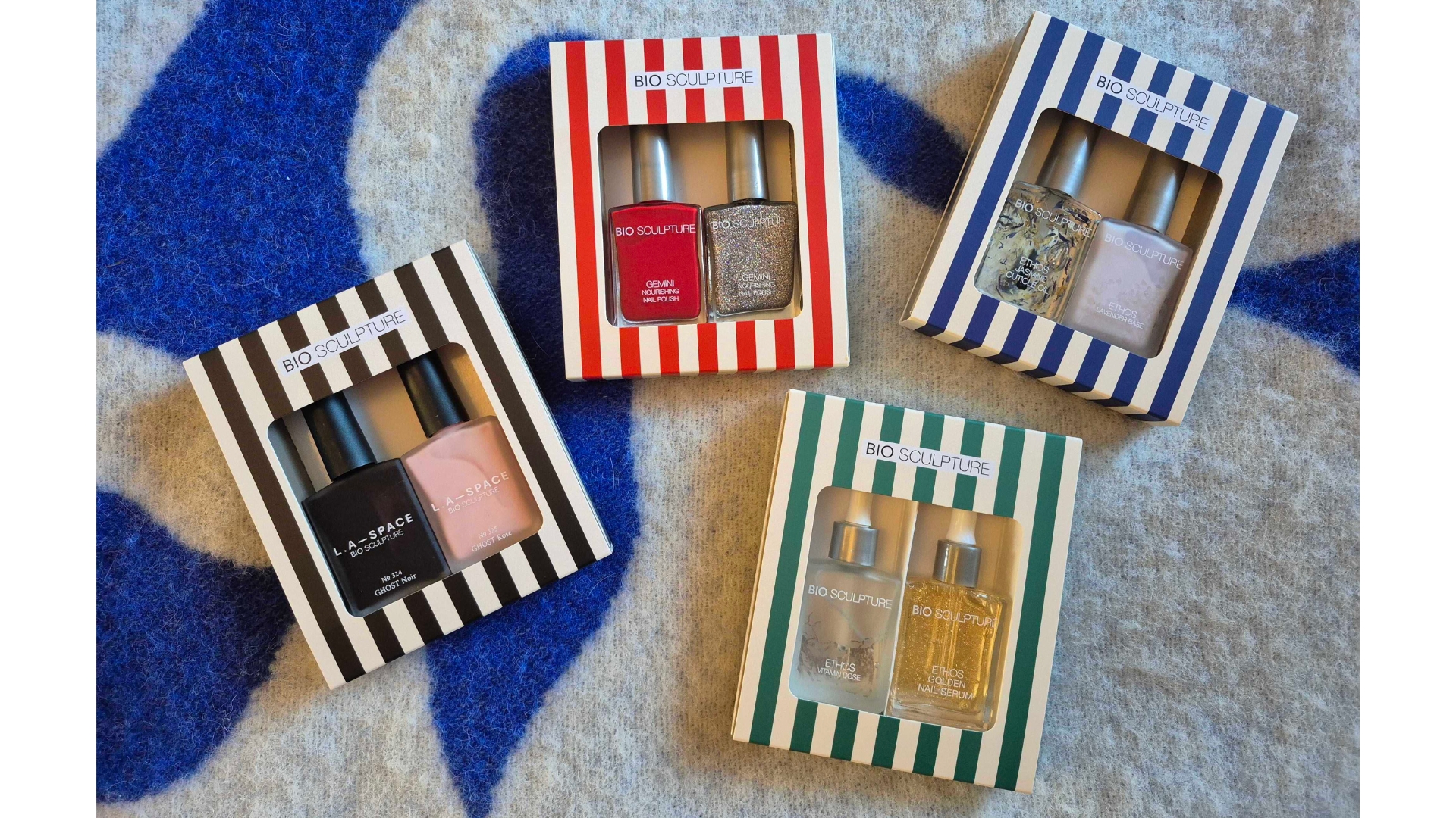An array of Bio Sculpture nail polish and care duo gift sets, pictured in their stripey festive boxes and laid out over a blue and white blanket background