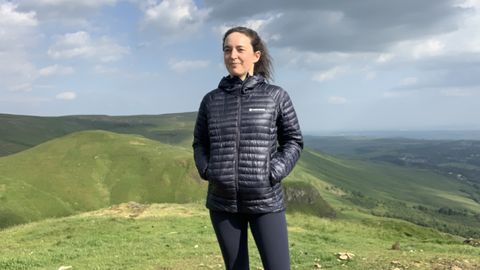 A hiker wearing a blue down jacket looking at the view of the mountains