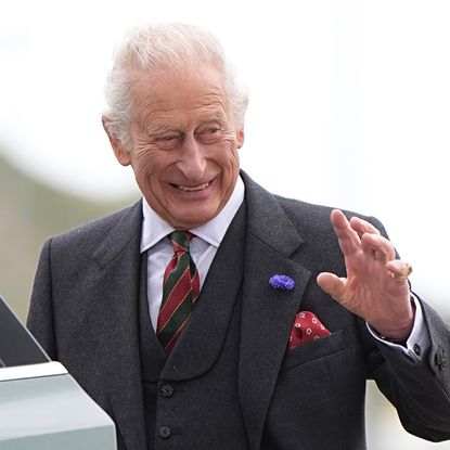 King Charles waving and smiling while getting into a car