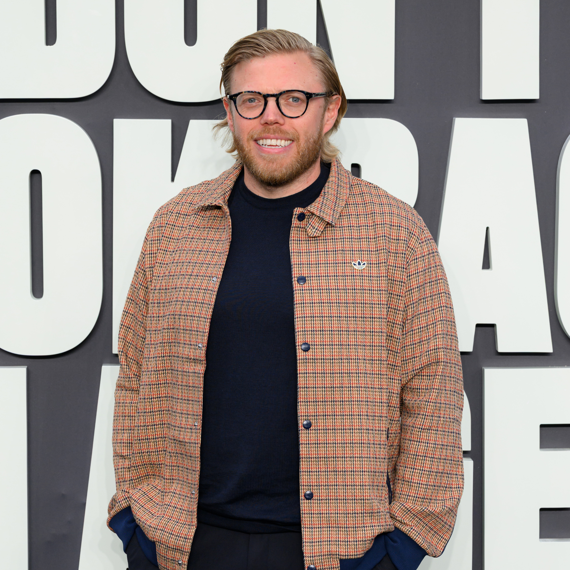 Rob Beckett in beige check shirt and black t-shirt at Oasis Don't Look Back In Anger premier.