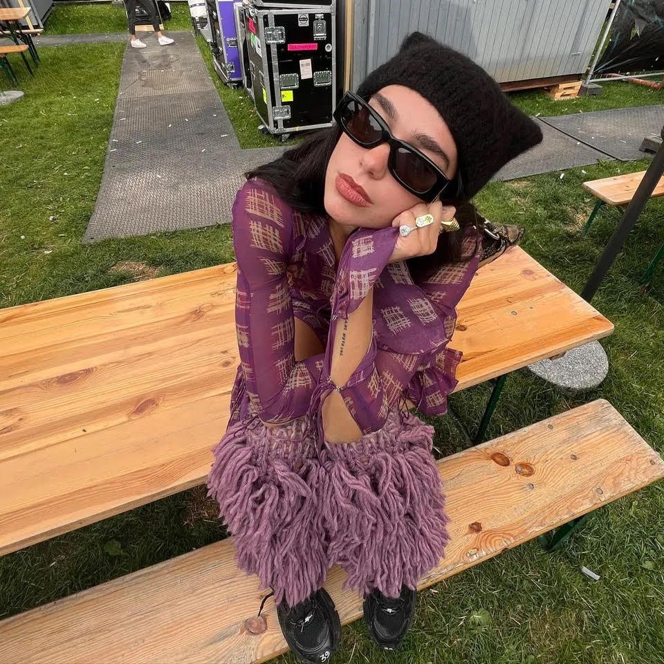 Dua lipa wears a purple top black beanie, black sunglasses and Walton Emma rings.