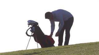 A golfer searching through a pocket in their golf bag