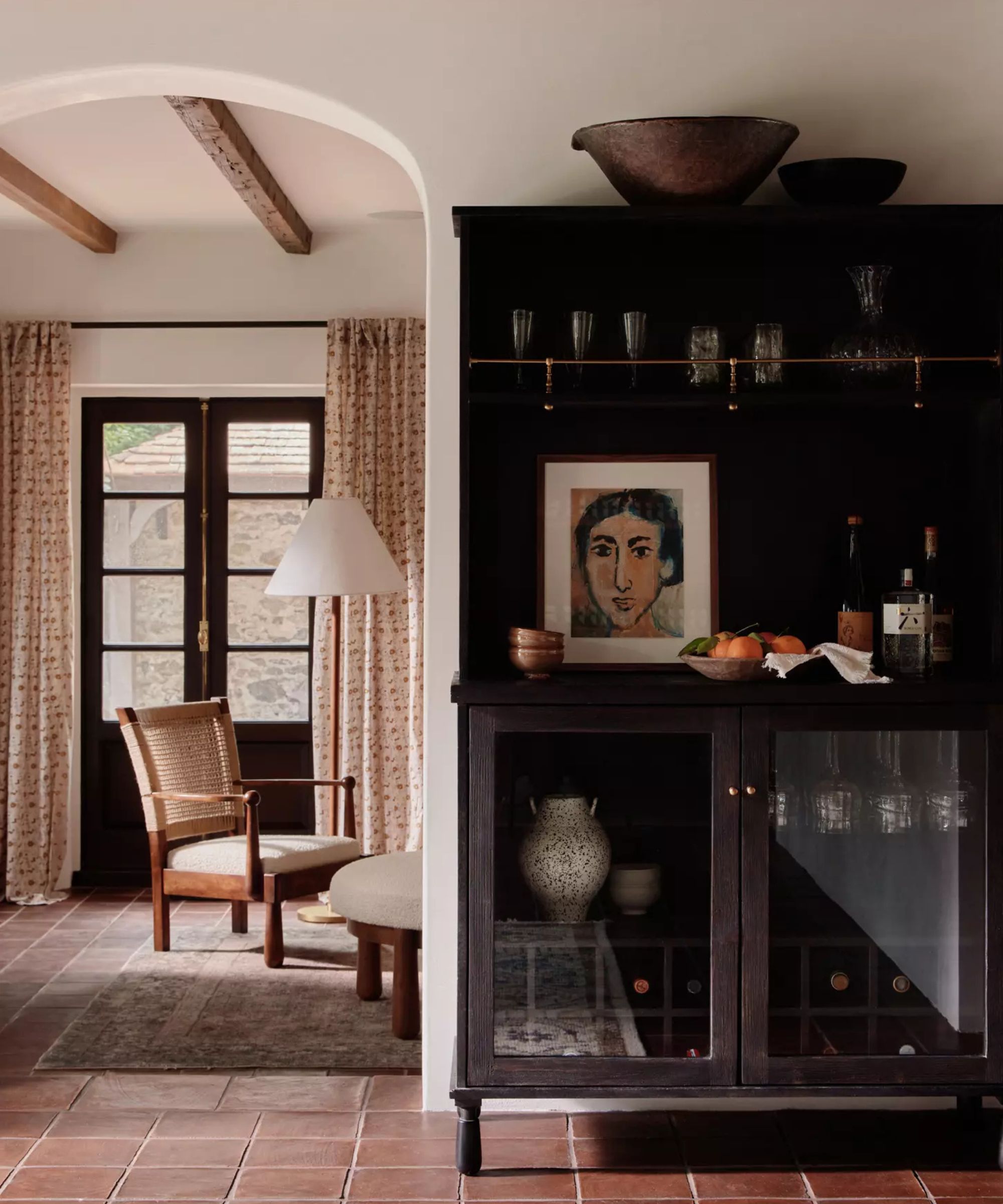 A white traditional kitchen with a dark wood freestanding cabinet featuring glass doors and a brass shelf rail