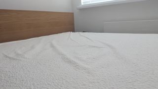 A white mattress protector on a bed with a wooden headboard