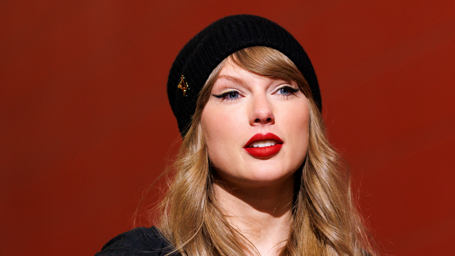 Taylor Swift wearing a red lip color and beanie hat with her hair down.