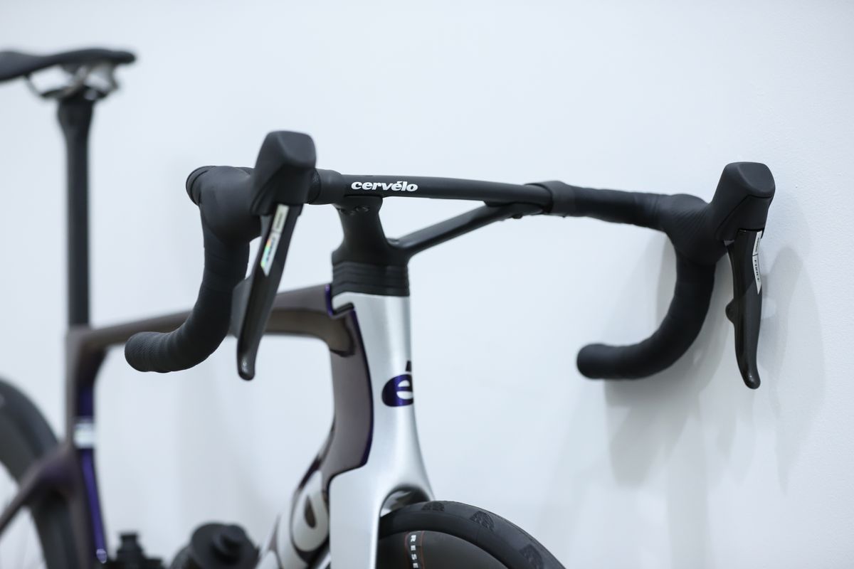 A blue and silver Cervelo S5 stands against a white wall