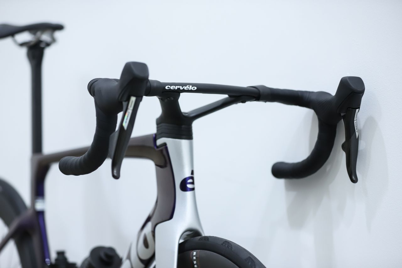 A blue and silver Cervelo S5 stands against a white wall