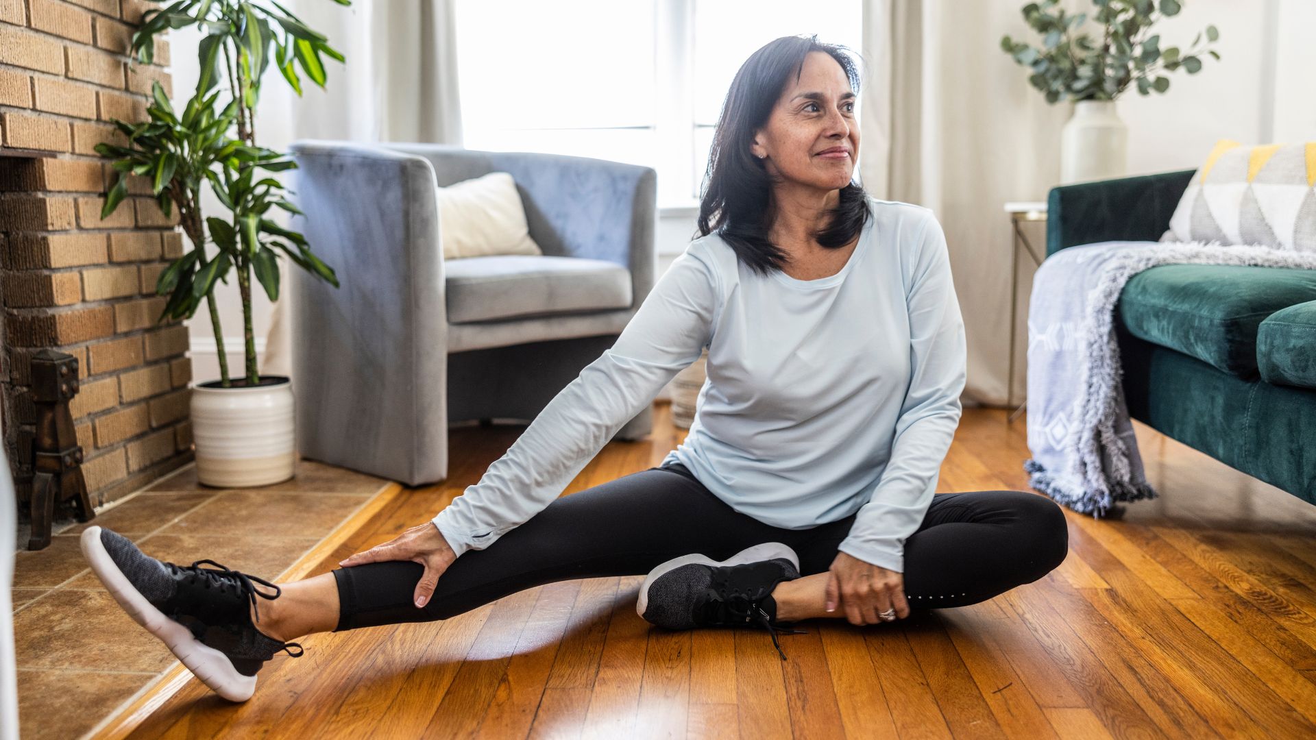 Woman stretching hamstrings on wooden floor at home to set up for Romanian deadlift exercise