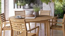 A circular wooden outdoor dining table and five dining chairs on a patio terrace