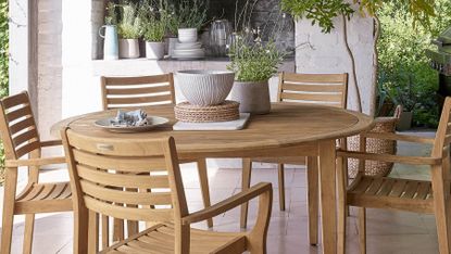 A circular wooden outdoor dining table and five dining chairs on a patio terrace