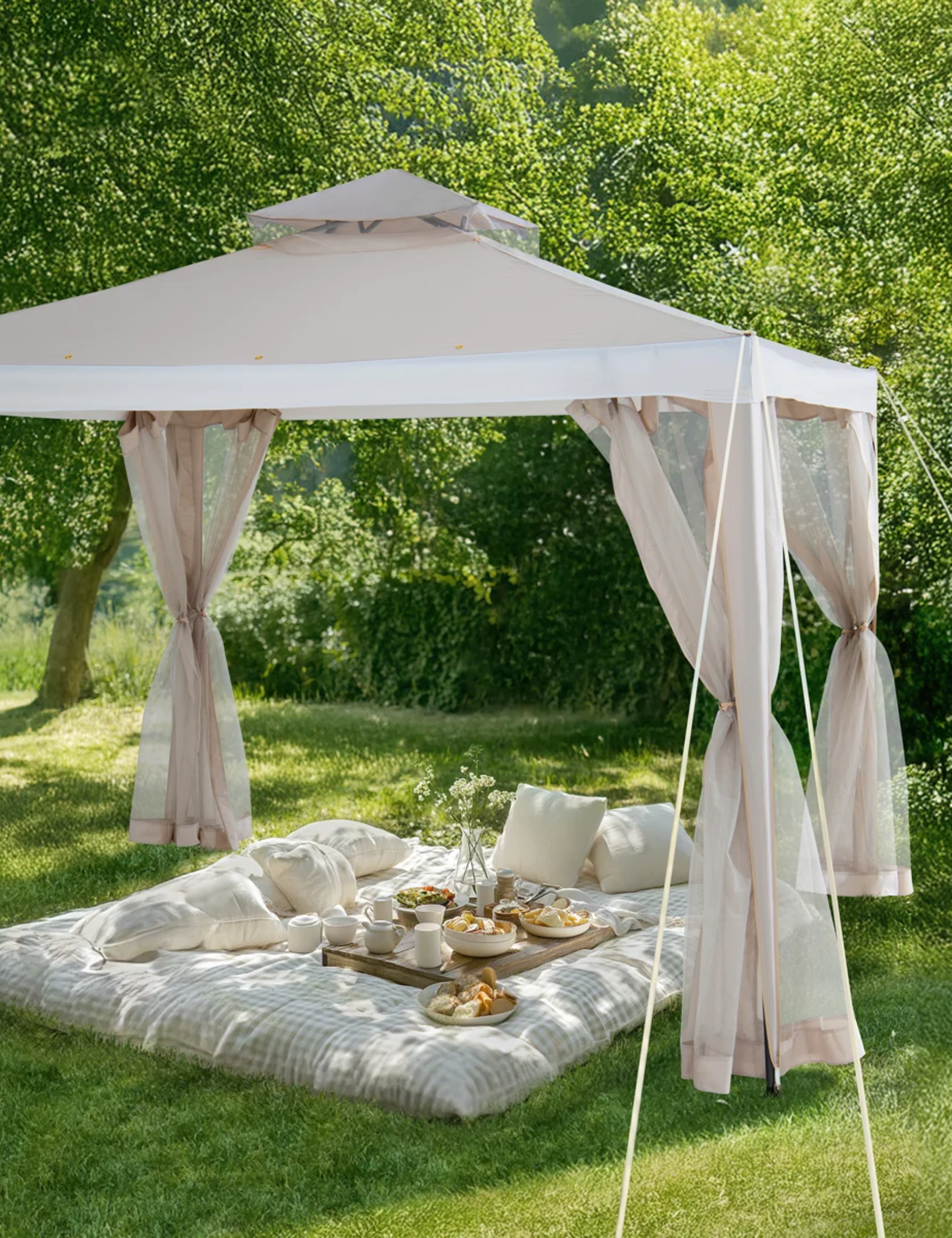 Beige soft-top gazebo with mesh standing over a charming picnic scene on a grassy lawn surrounded by trees
