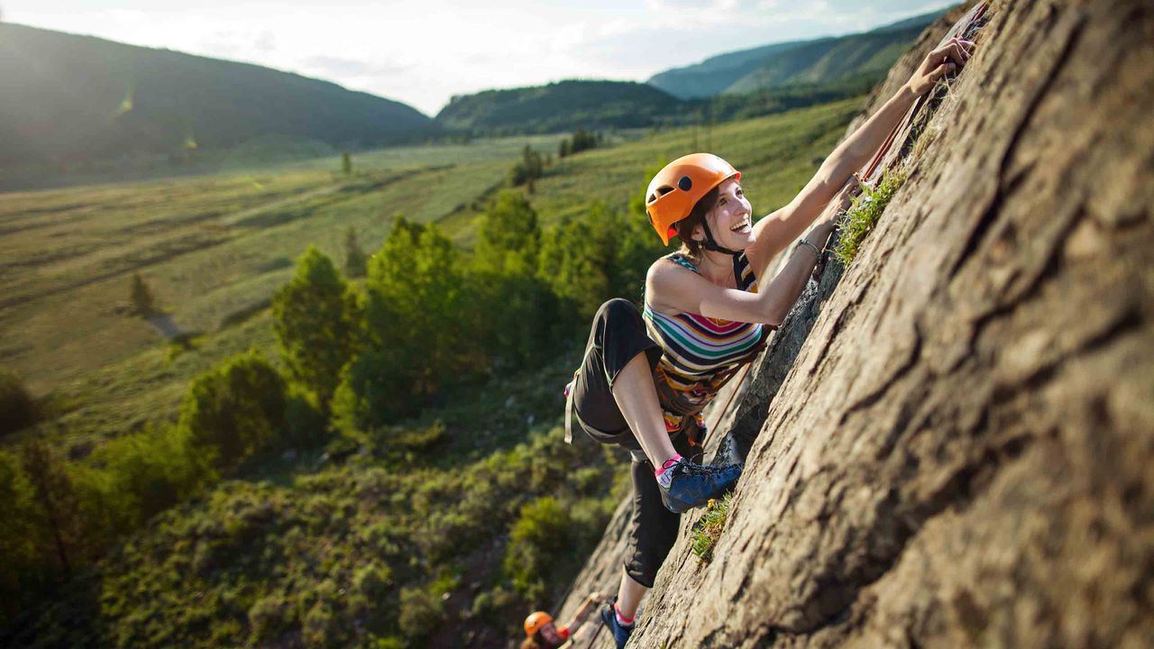 A woman climbs up the side of a mountain