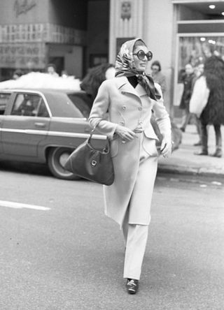 Jackie O crossing a street in her iconic glasses and headscarf