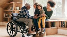 A woman and her two young kids visit with the kids' grandmother, who is in a wheelchair. 