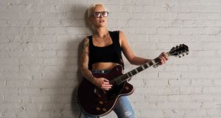 Carmen Vendenberg leans against a white wall with Gretsch semi-hollow