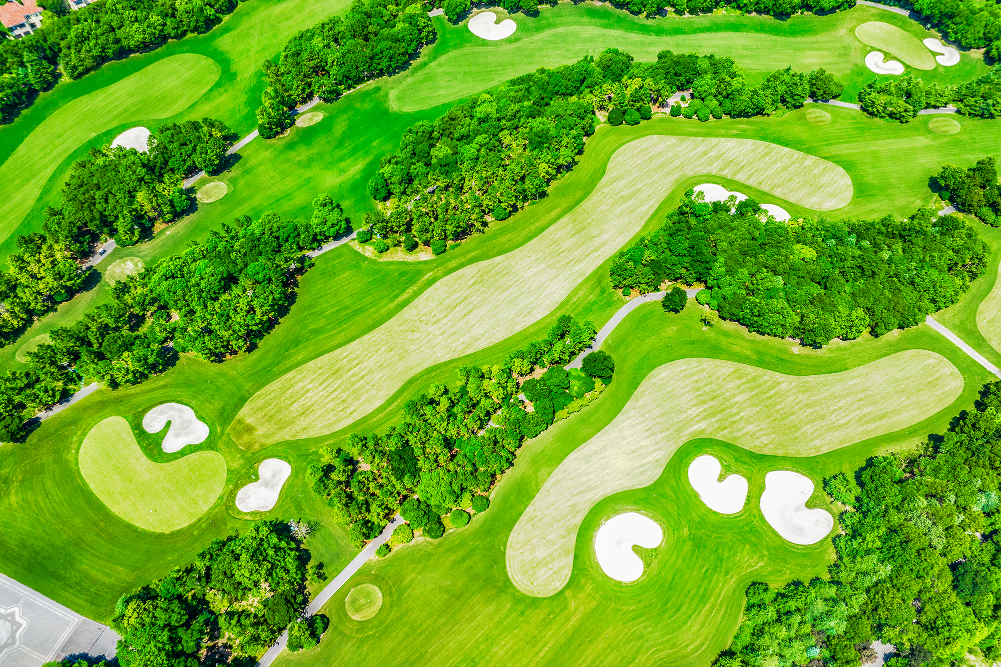 Aerial view of a golf course, showing four different holes with fairways, greens, bunkers and lots of trees