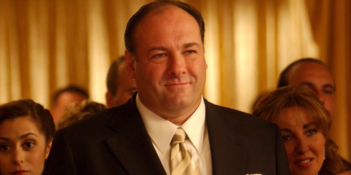 The Sopranos Tony wearing a black suit, white shirt, and gold striped tie in a crowd