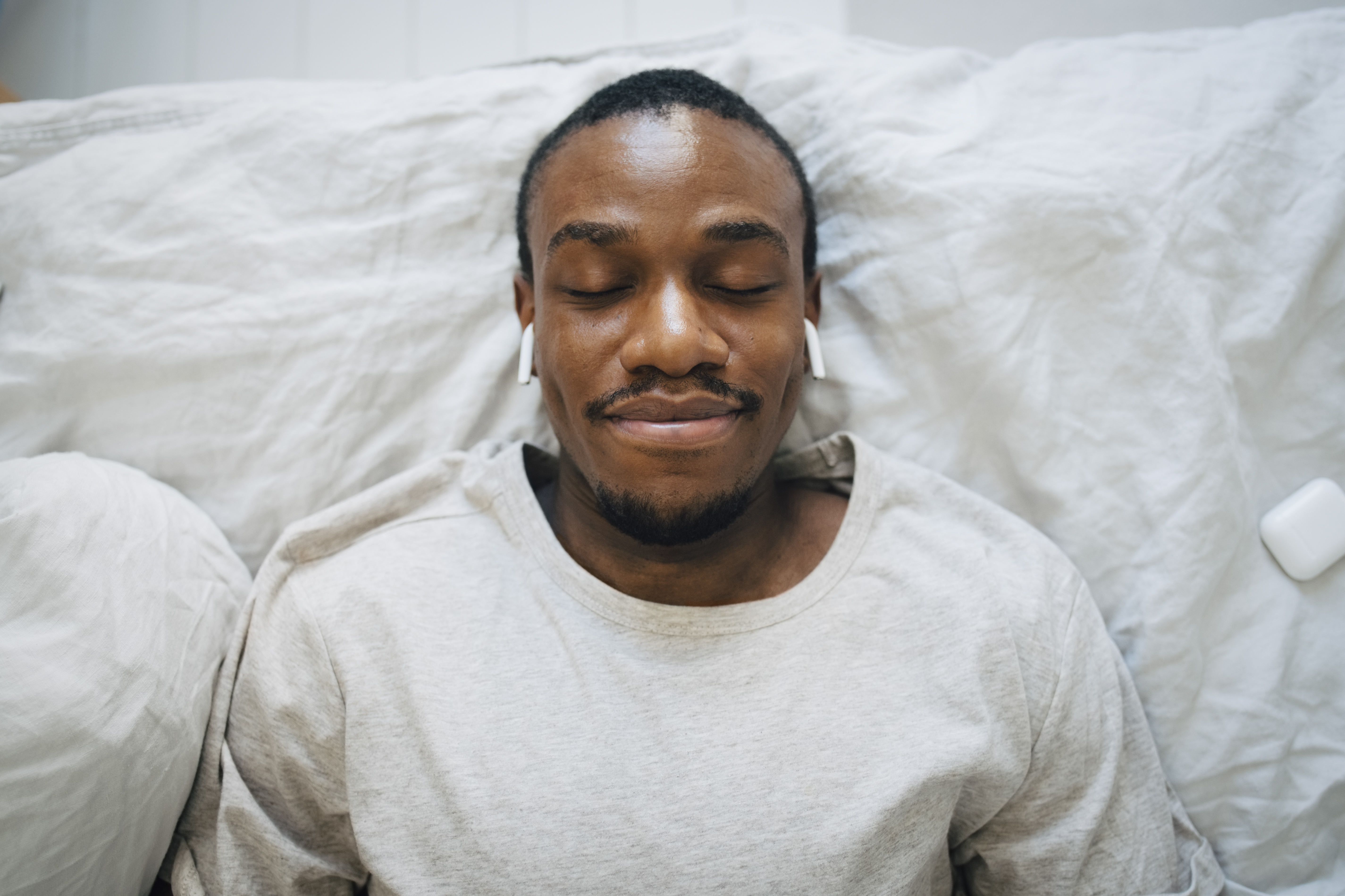 Person with their eyes closed in bed while wearing Apple AirPods