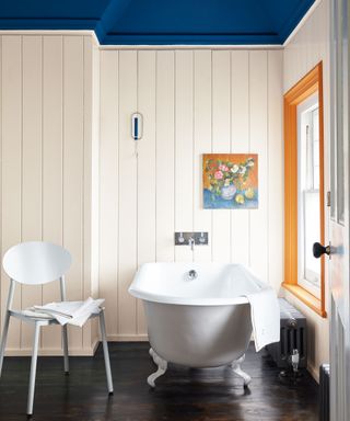 Bathroom with blue painted ceiling, orange window frame, bath, chair