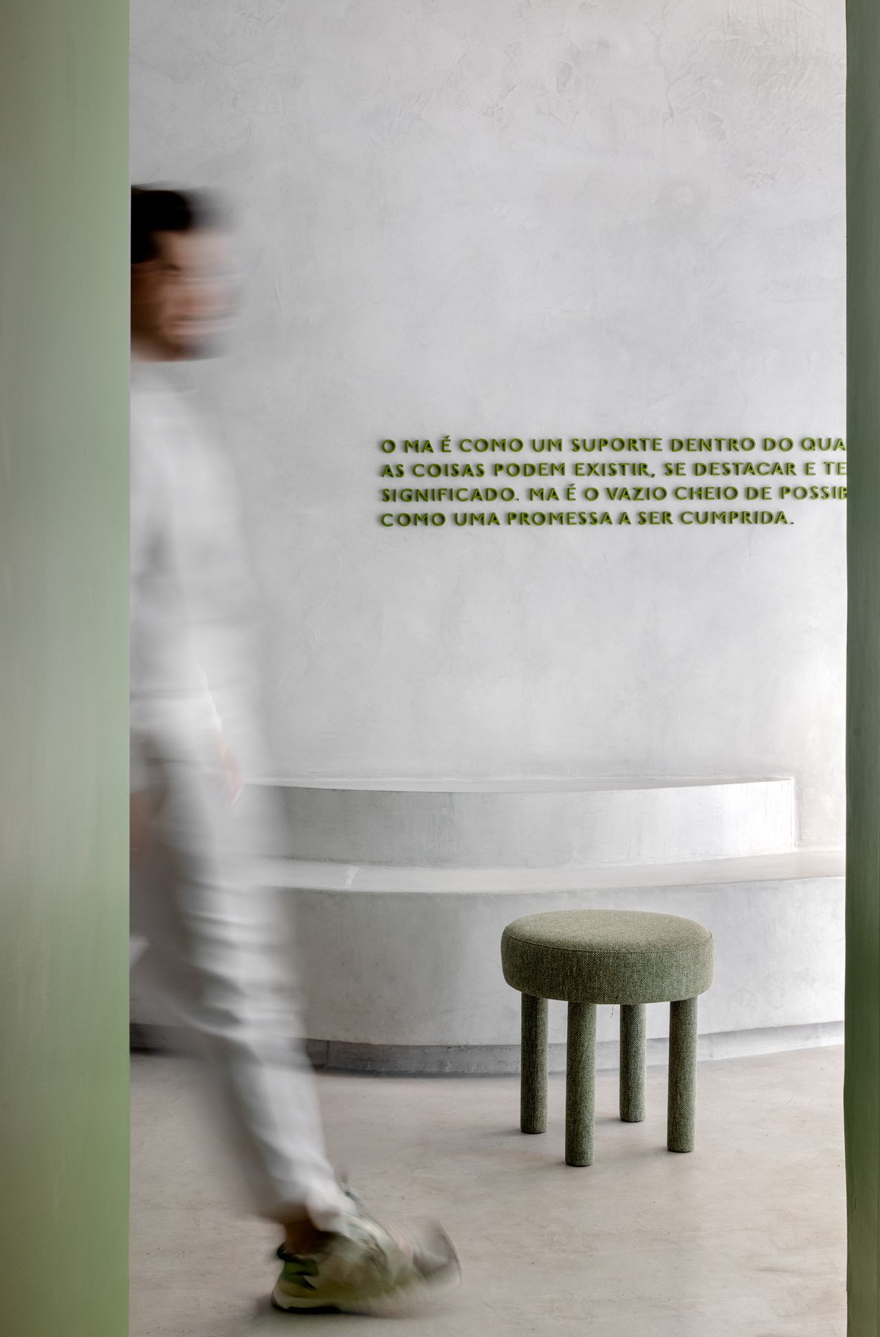 A white-washed, plastered matcha cafe with sculptural decor features monochromatic furnishings and an emerald green and chrome bar counter.