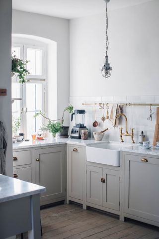 A small grey kitchen with storage rails, a Belfast sink and white countertops with cabinets on legs