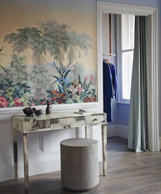 A marble dressing table with a gray stool backed by tropical wallpaper