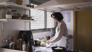 A woman chopping vegetables next to the sink with an air fryer on the side