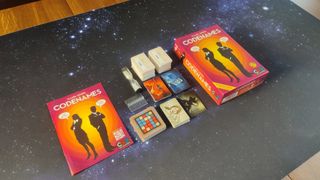 Codenames box, instructions, cards, and timer laid out nearly in a row on a starry background