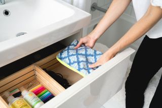 open drawer of bathroom sink storage with compartments and make up bag