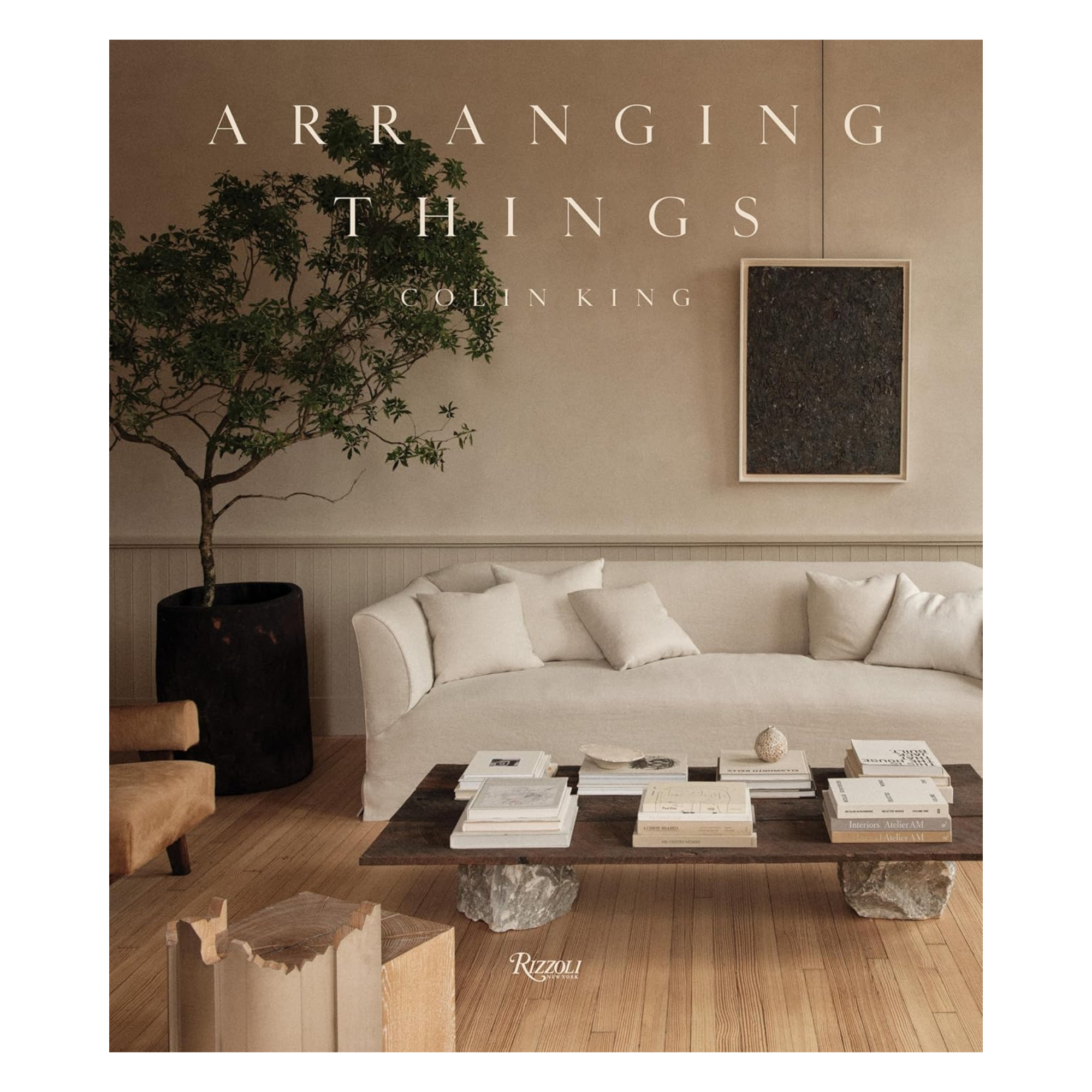 a book titled "Arranging Things" with an image of a white couch and a coffee table on the cover next to an indoor tree