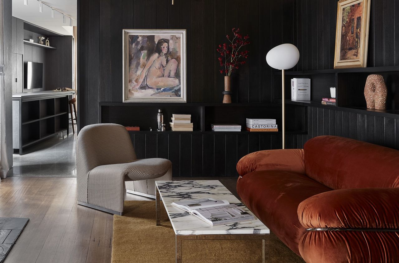 A living room with black walls, a red sofa and a gray chair