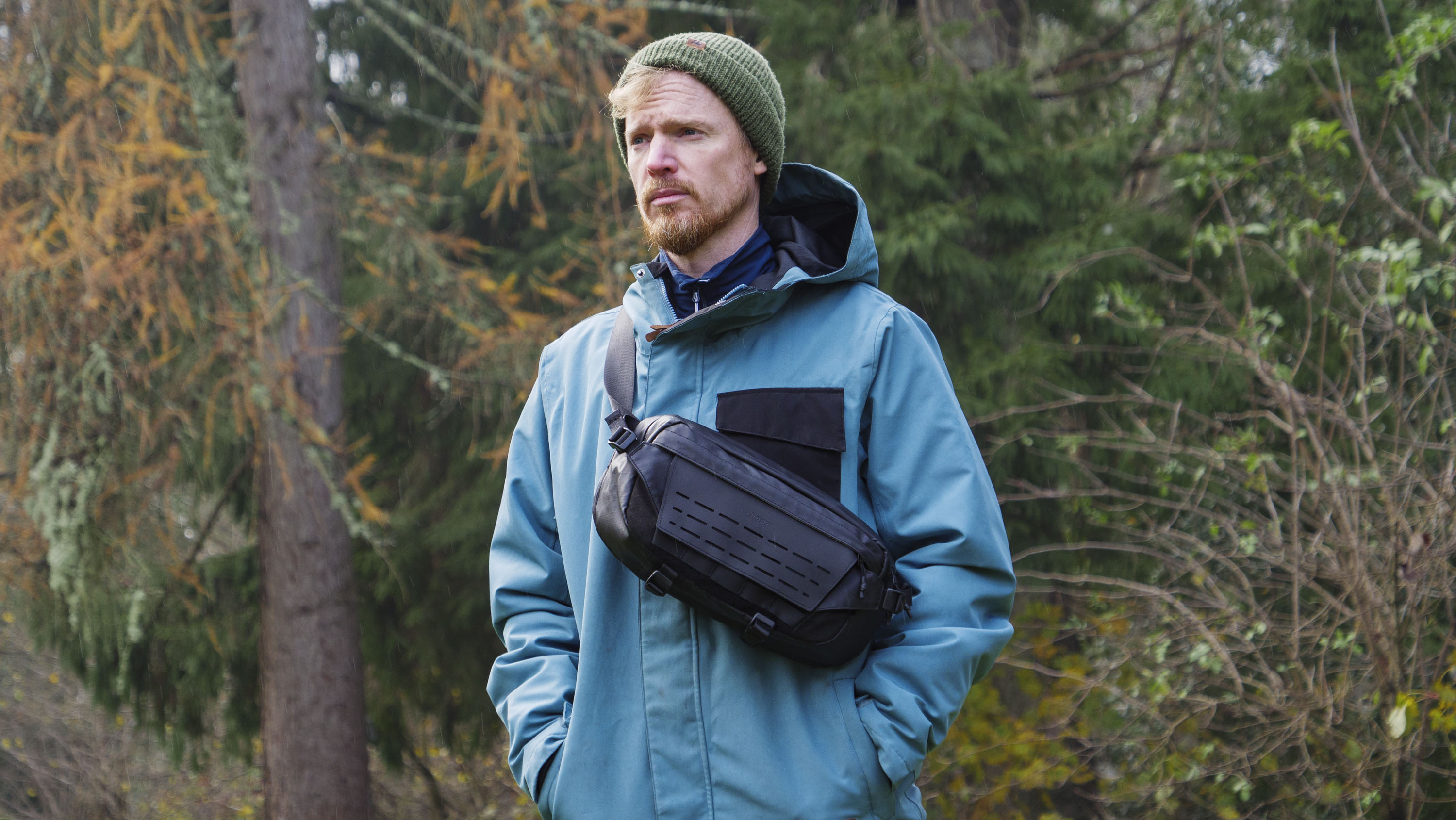 Man wearing a blue jacket outside with a Ulanzi Camera Sling Bag over his shoulder and resting on his midriff