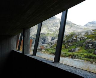 View of the landscape through openings of the Trollstigen Visitor Centre. Mountains, rocks, greenery and a river can be seen under a clear white sky