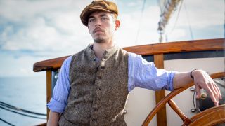 Hero Fiennes Tiffin stands leaning at the wheel of a boat in The Ministry of Ungentlemanly Warfare.