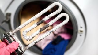 Washing machine heating element covering in limescale being held by an open washing machine door
