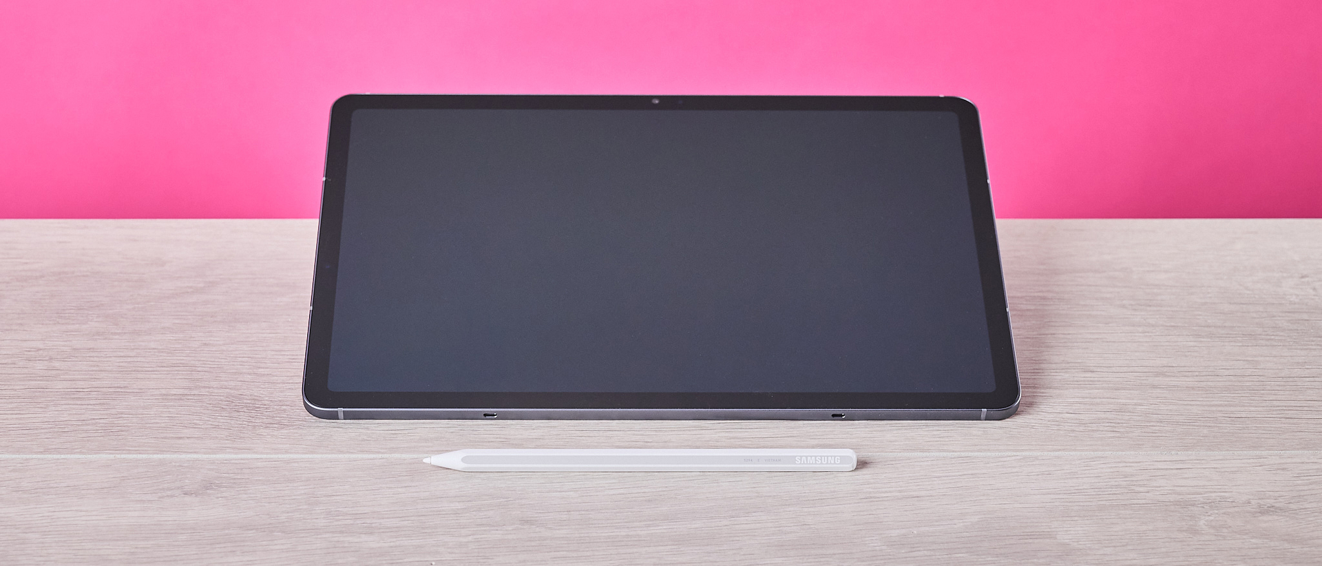 Front view of Samsung Galaxy Tab S11 and S Pen, on a desk with pink wall in background