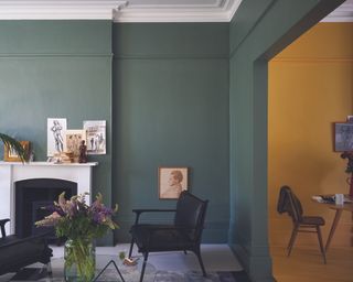a living room painted in Wimborne White No.239 Estate Emulsion, Green Smoke No.47 Estate Emulsion & Modern Eggshell India Yellow No.66 Modern Emulsion & Modern Eggshell – with a white fireplace, art on the walls, and black chairs, and a vase full of flowers on a glass coffee table