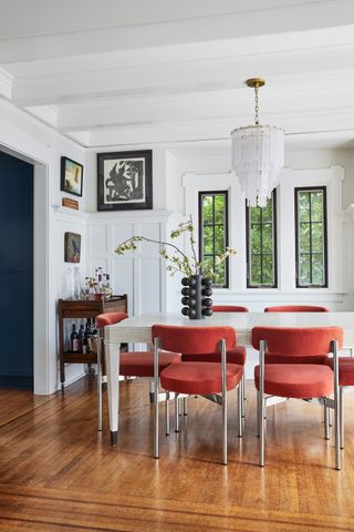 A white dining room with wainscoting across the walls and red dining chairs