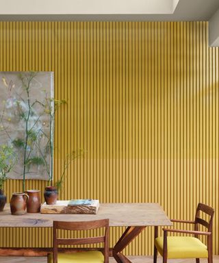 yellow dining room with painted slatted wall behind, artisan style table and chairs, earthenware on table, artwork
