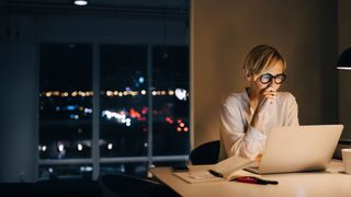 Woman working late at night in kitchen light with laptop and books