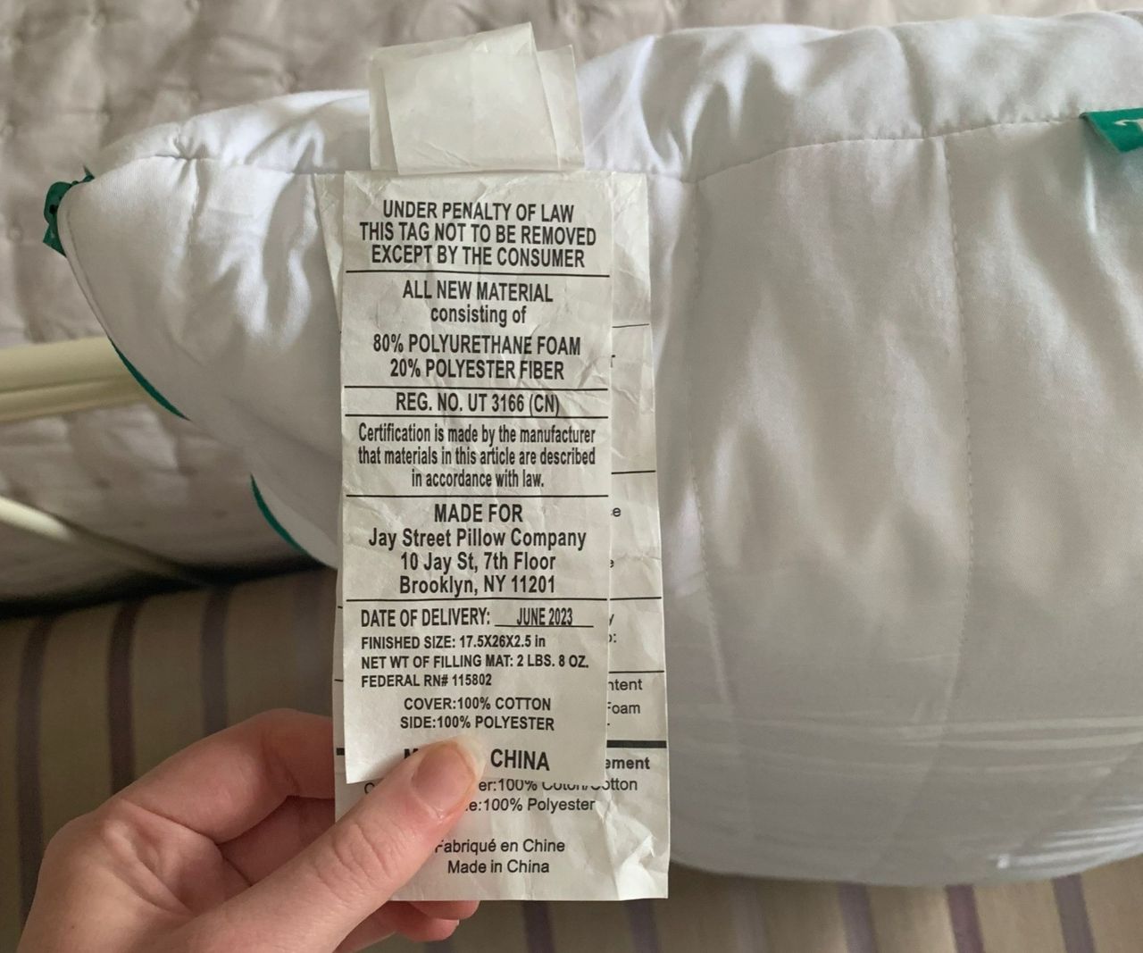 A hand holding the care tag of the Marlow Pillow.