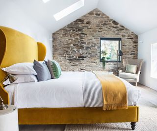 Yellow velvet bed, white bedding, stone wall