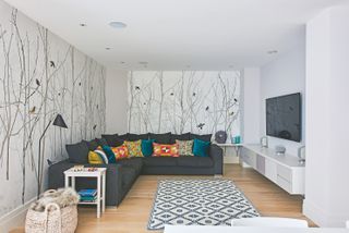 Basement with sectional sofa and TV and white walls with mural, wood floor and rug