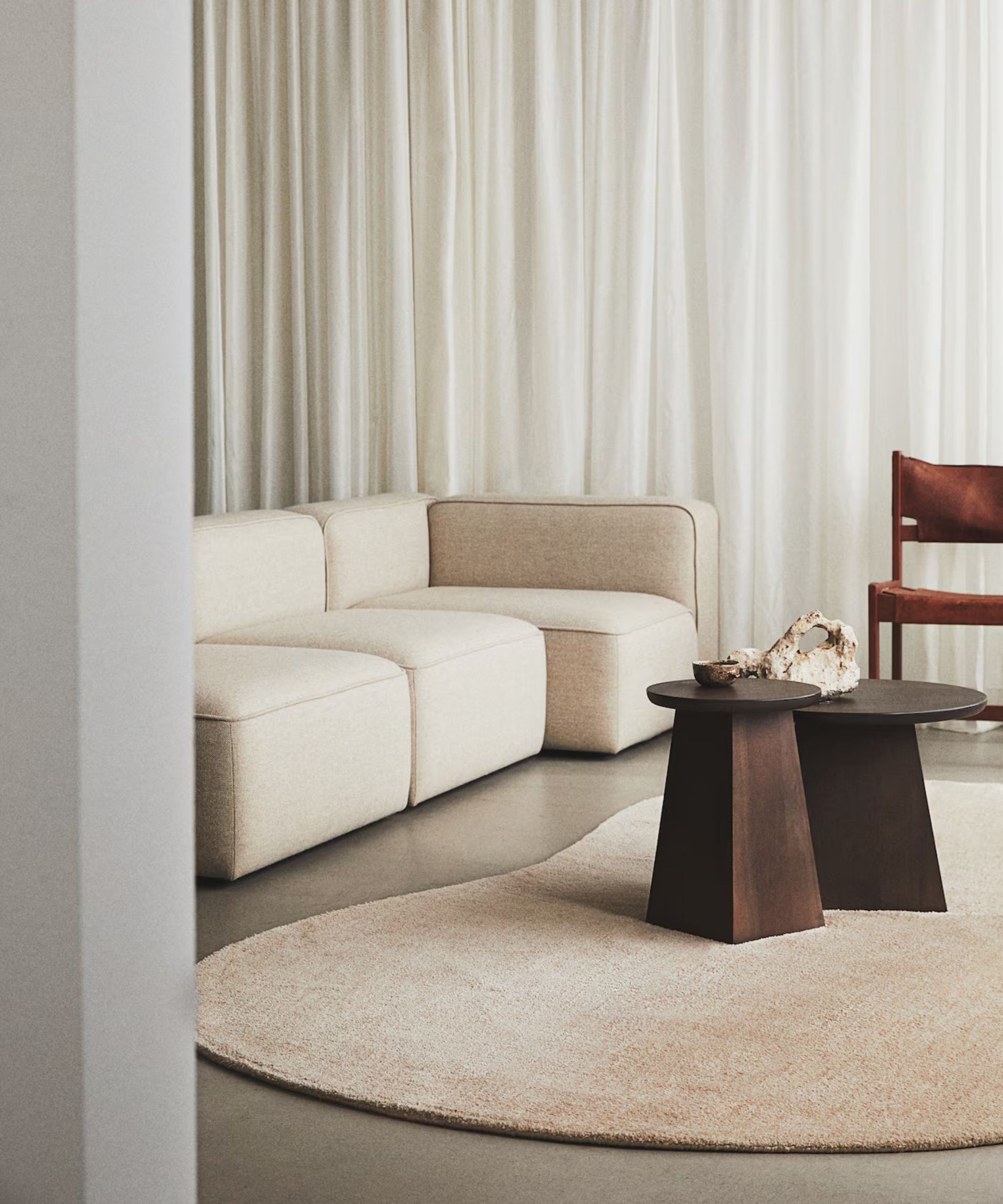 minimalist neutral living room with floor to ceiling drapes, a beige cube modular sofa, abstract shape rug, dark wood side tables